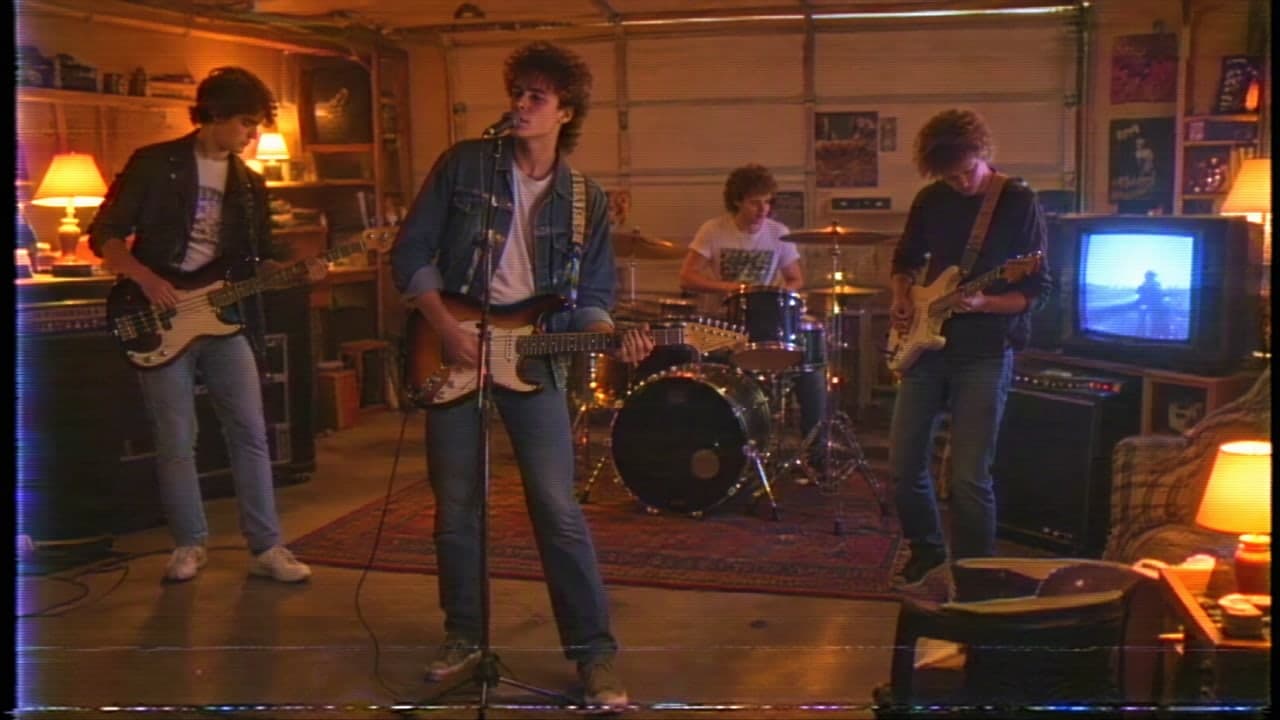 A band playing in a lamp-lit garage, with soft tape grain and an old TV glowing.